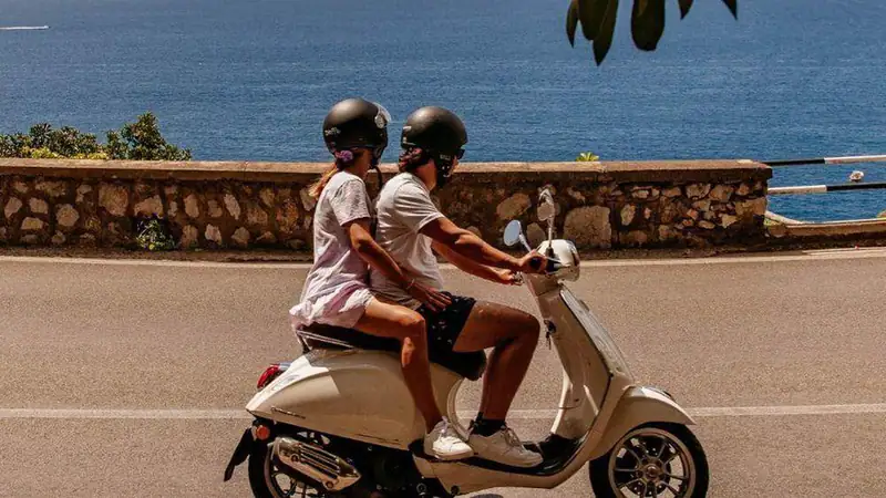 A couple riding a cream scooter along the coast road